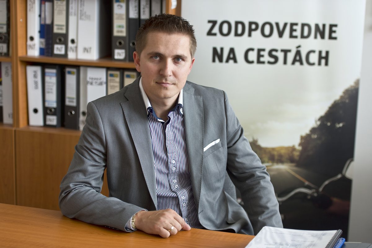 Milan Troška za stolom v kancelárii, za ním banner Zodpovedne na cestách