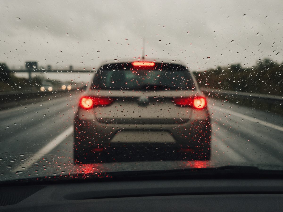 Pohľad cez daždivé sklo na blízko idúce auto s brzdovými svetlami